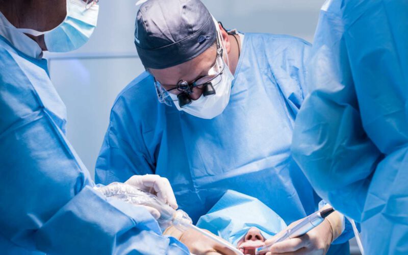 A male dentist in uniform perform dental implantation operation on a patient at dentistry office.
