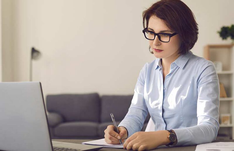 Concentrated woman watching online workshop or attending continuing education webinar on laptop computer. Focused employee with attention to detail studying new information