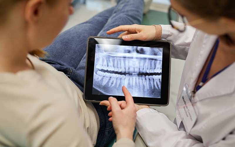 Rear view of doctor showing x-ray of teeth on digital tablet to the patient at dental clinic